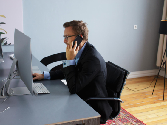 Un homme au téléphone travail à son bureau devant son écran d'ordinateur en tenant sa souris dans la main