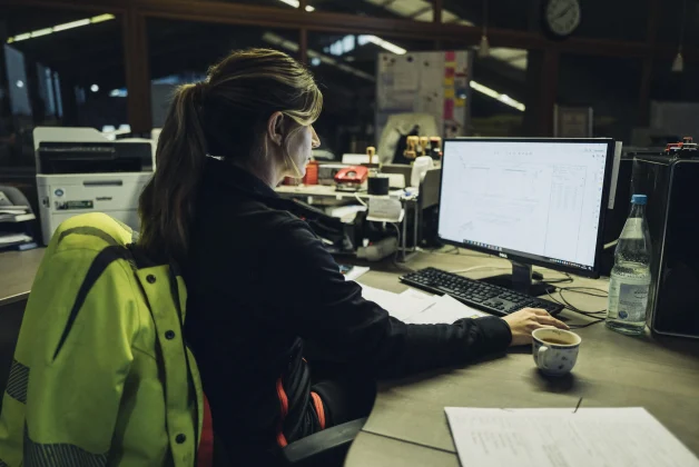 Une femme est devant son écran en train de travailler, elle est assise devant son bureau