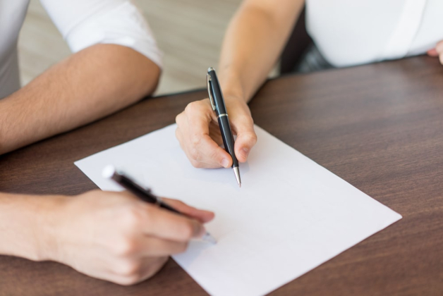 Deux personnes écrivent quelque chose sur un document en papier posé sur une table