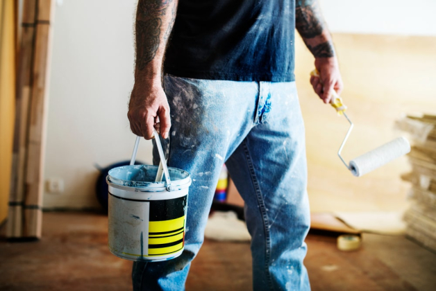 Un homme peintre marche avec un pot de peinture et un rouleau sur son chantier de travail