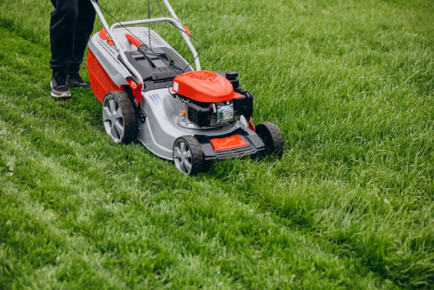 Un paysagiste est en train de passer une tondeuse orange sur une pelouse d'herbe verte