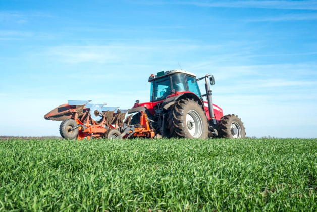 Un tracteur rouge avec une machine agricole est dans un champ vert