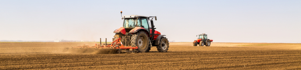 Un tracteur rouge passe une machine dans un champ pour retourner la terre