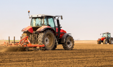 Un tracteur rouge passe une machine dans un champ pour retourner la terre
