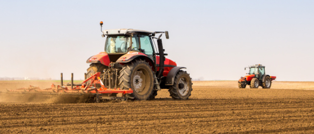 Un tracteur rouge passe une machine dans un champ pour retourner la terre