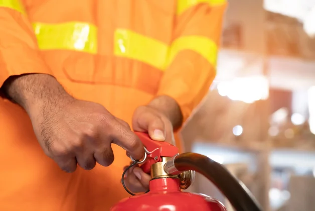 Un homme en tenue de sécurité haute visibilité orange est en train d'utiliser un extincteur