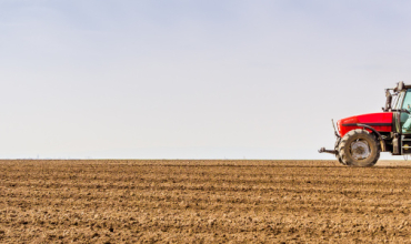 Un tracteur seul dans un champ ensoleillé passe sa herse dans la terre
