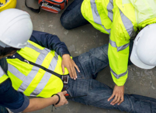 Plusieurs ouvriers en gilet de haute visibilité jaune surveille un collègue par terre