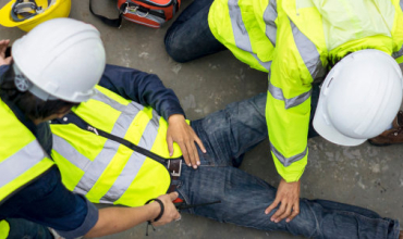 Plusieurs ouvriers en gilet de haute visibilité jaune surveille un collègue par terre