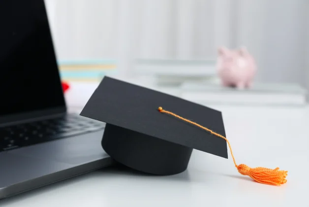 Un ordinateur et un chapeau de diplômé sont posés sur une table blanche