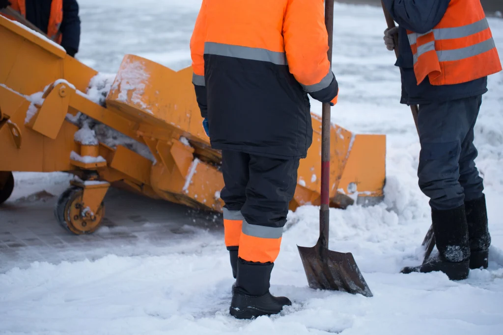 Deux ouvriers en tenue de haute visibilité orange sont en train de déblayer de la neige avec des pelles