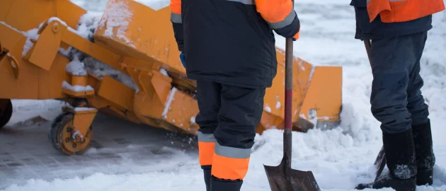 Deux ouvriers en tenue de haute visibilité orange sont en train de déblayer de la neige avec des pelles