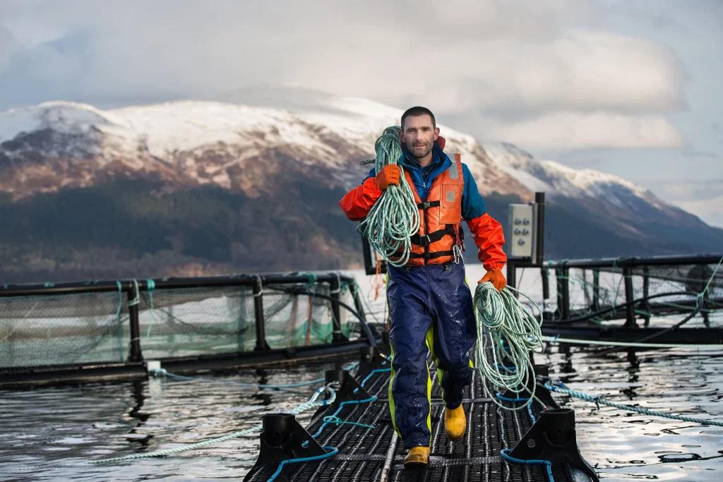 Un homme en tenue hivernale haute visibilité travail dans une ferme à saumon en hiver