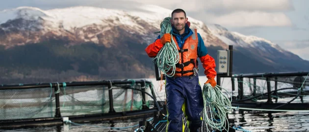 Un homme en tenue hivernale haute visibilité travail dans une ferme à saumon en hiver